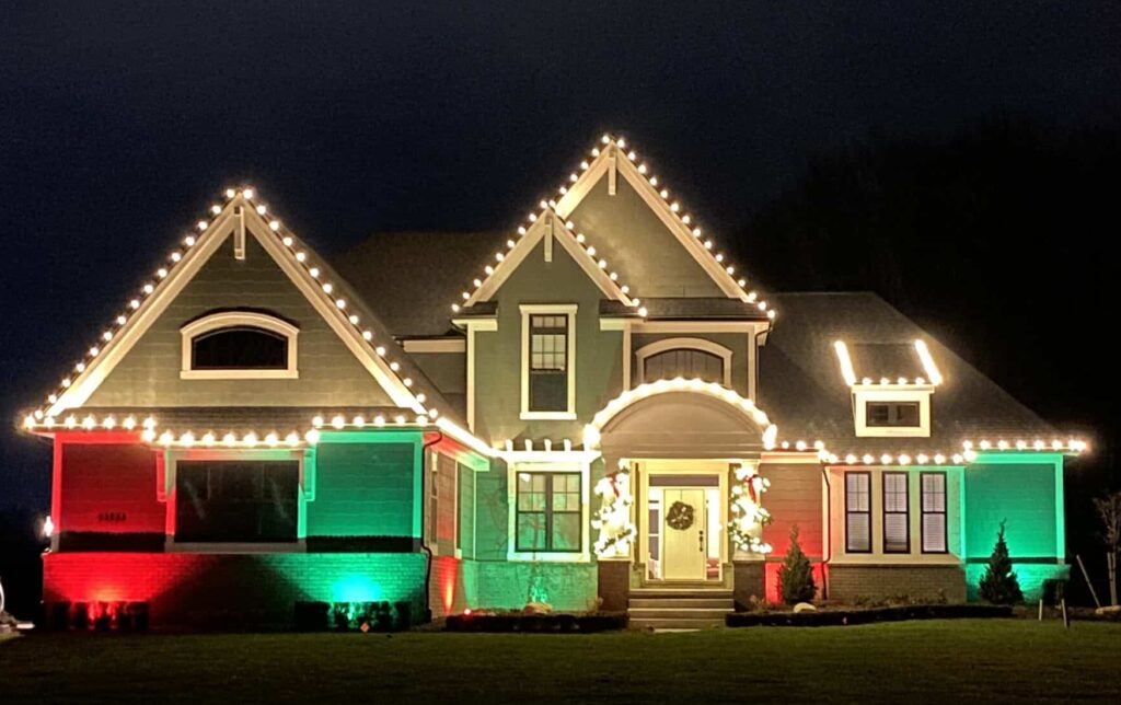 Festive house adorned with Christmas lights. White lights line the roof, while red and green spotlights illuminate the walls, creating a colorful holiday display.